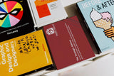 A collection of colorful book covers on design topics, fanned out on a white surface. Titles visible include "Graphic Design for Non-Profit Organizations," books on comic arts, and "The Strategic Advisor
